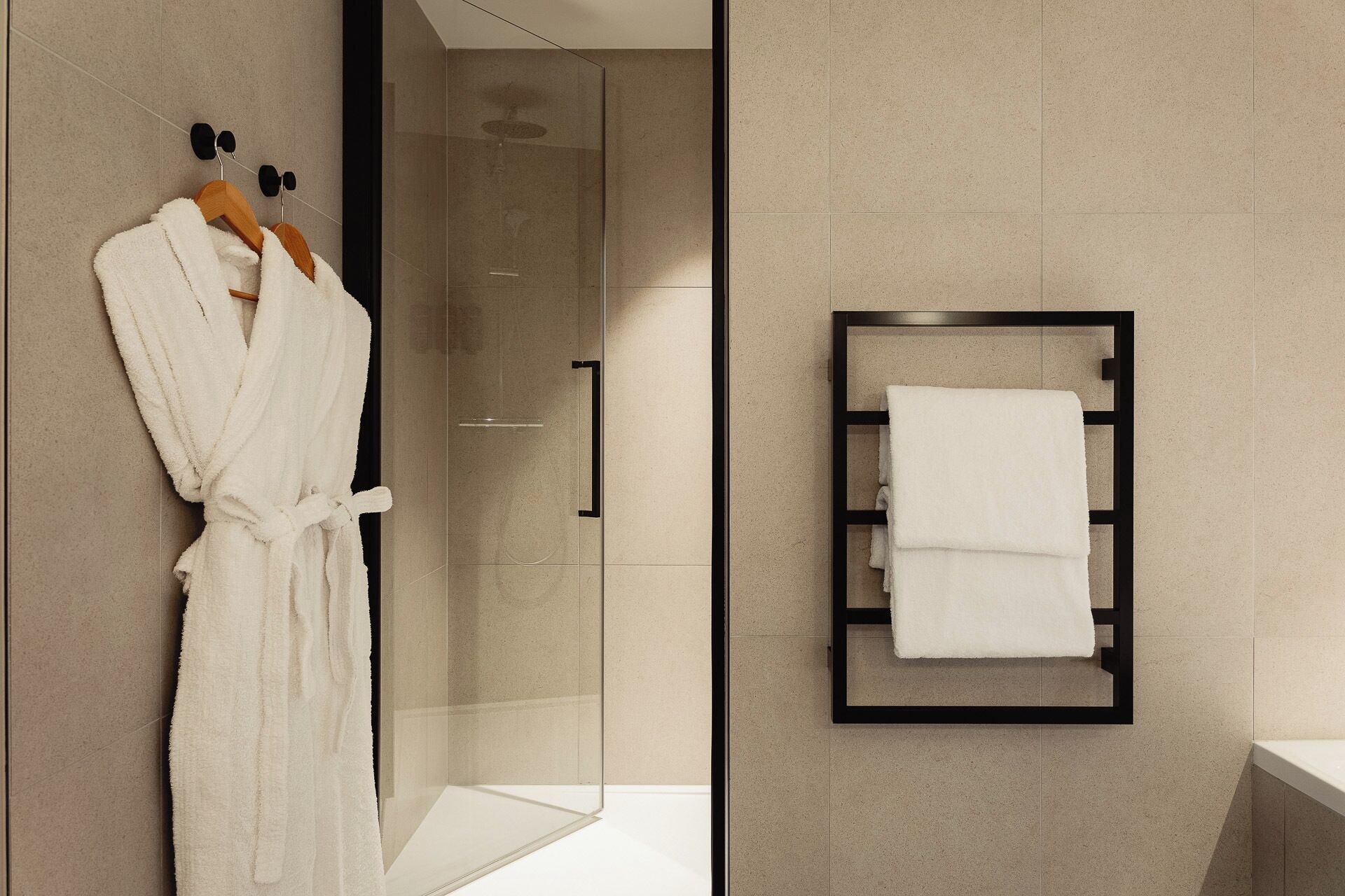 A modern bathroom with a glass shower enclosure, a wooden bathrobe rack, and a towel rack with a folded towel.