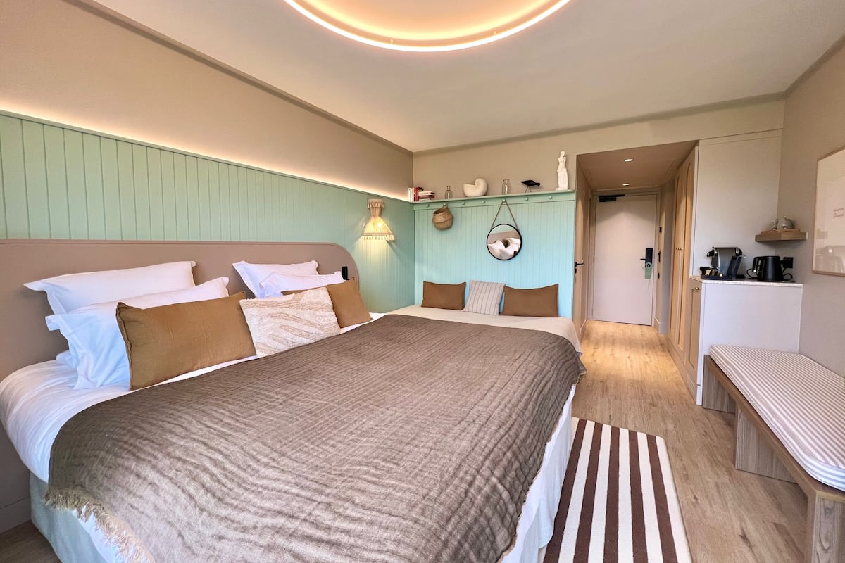 Une chambre avec un grand lit, des tables de chevet, un luminaire suspendu et une vue sur une autre pièce.