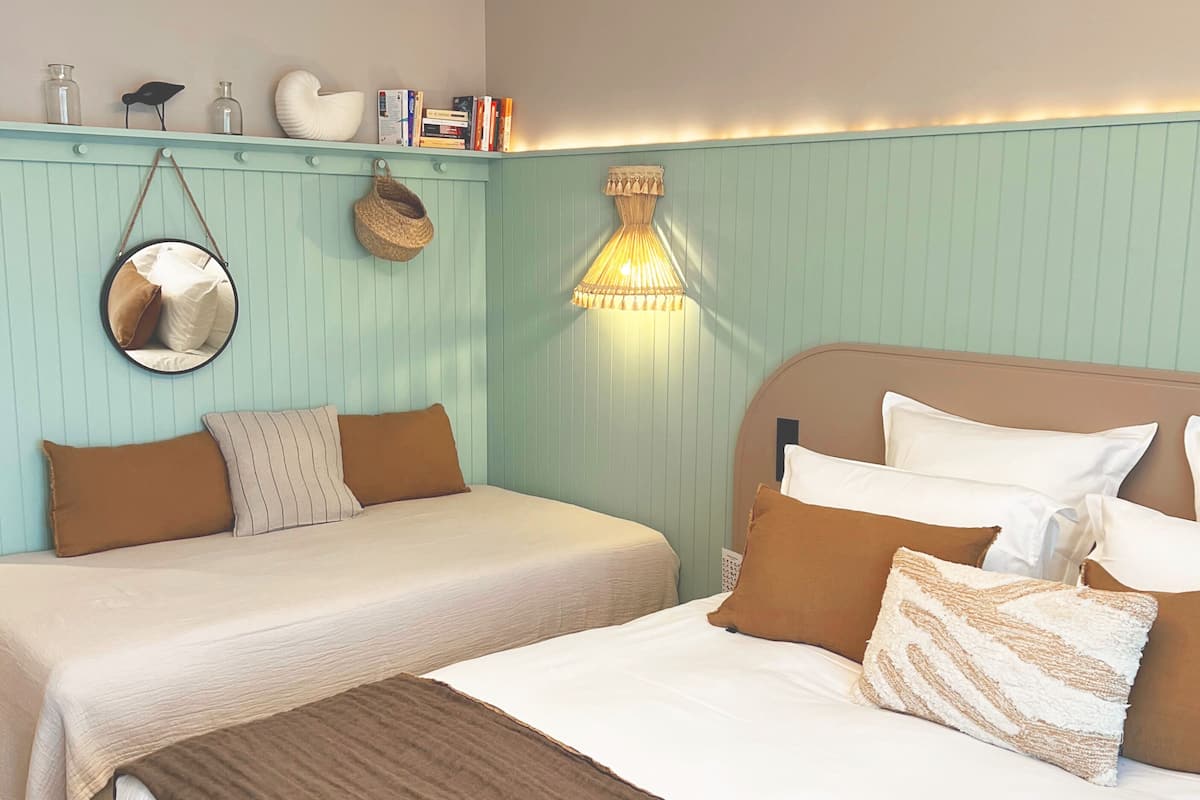 Une chambre avec deux lits, un miroir suspendu, une lampe fixée au mur et une étagère contenant des livres et des objets décoratifs.