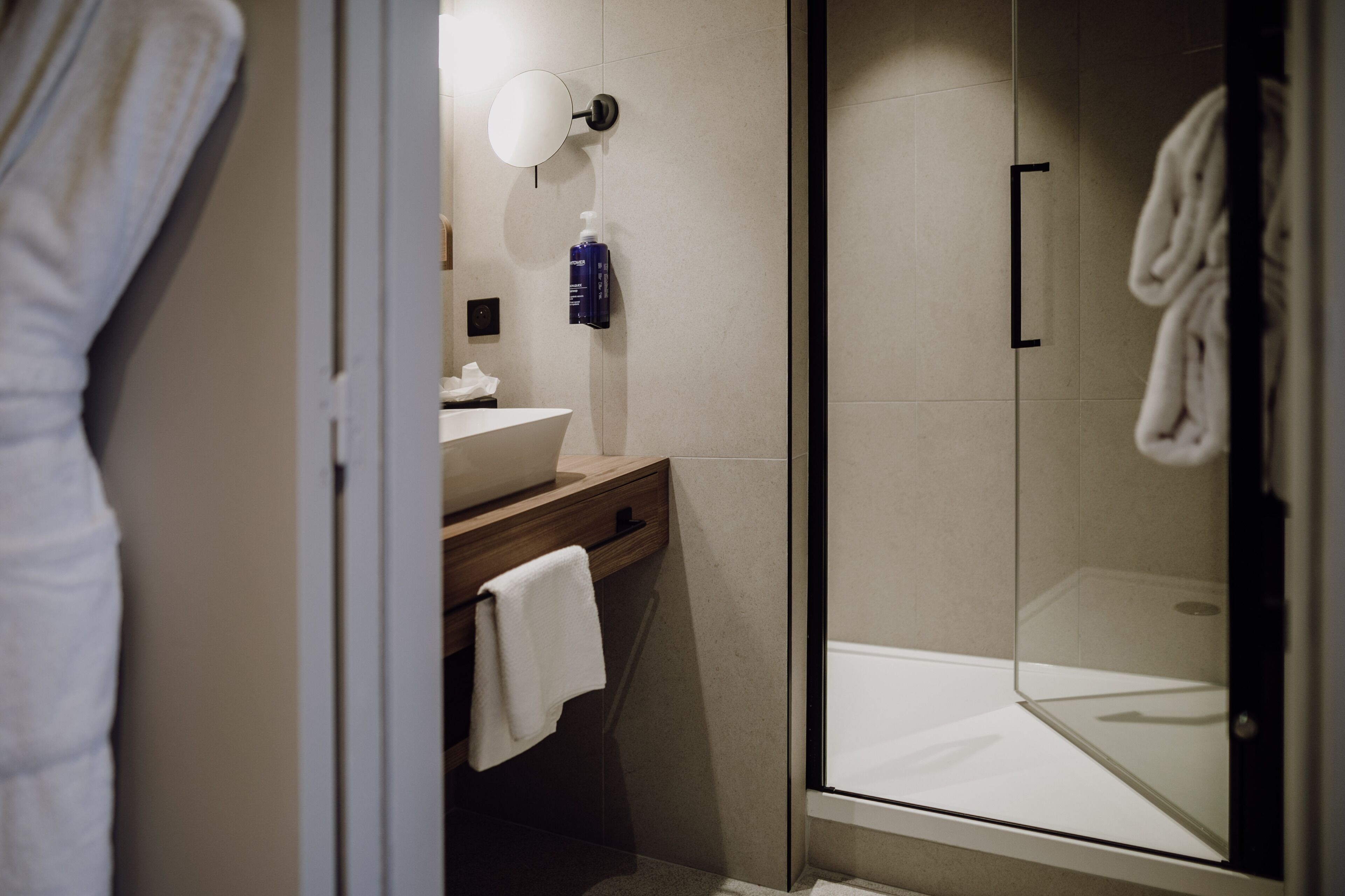 A modern bathroom with a glass shower enclosure, a wooden vanity, and a white sink.