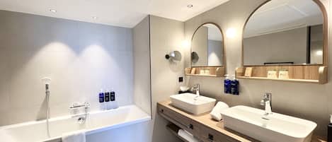 Un baño moderno con una bañera independiente grande, dos lavamanos y un mueble de tocador con espejo.