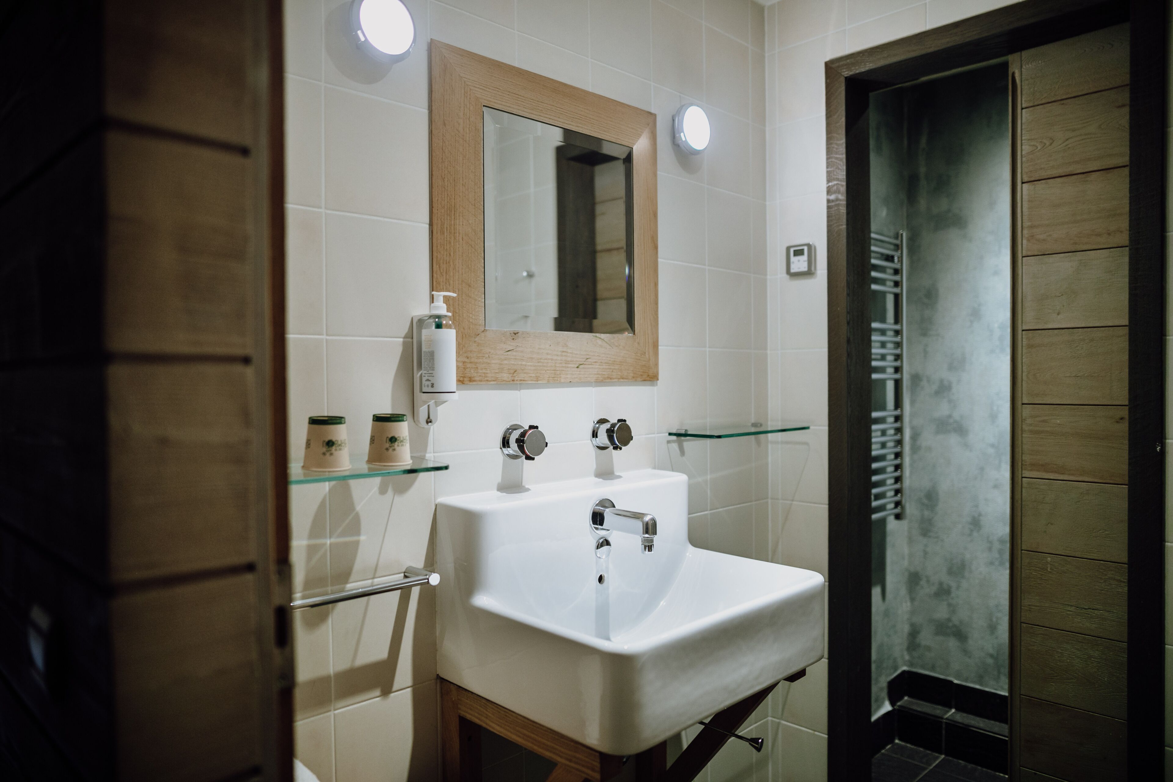 Een badkamer met een wit wastafelmeubel, een spiegel met houten lijst en een douchecabine met glazen wanden.