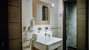 Een badkamer met een wit wastafelmeubel, een spiegel met houten lijst en een douchecabine met glazen wanden.