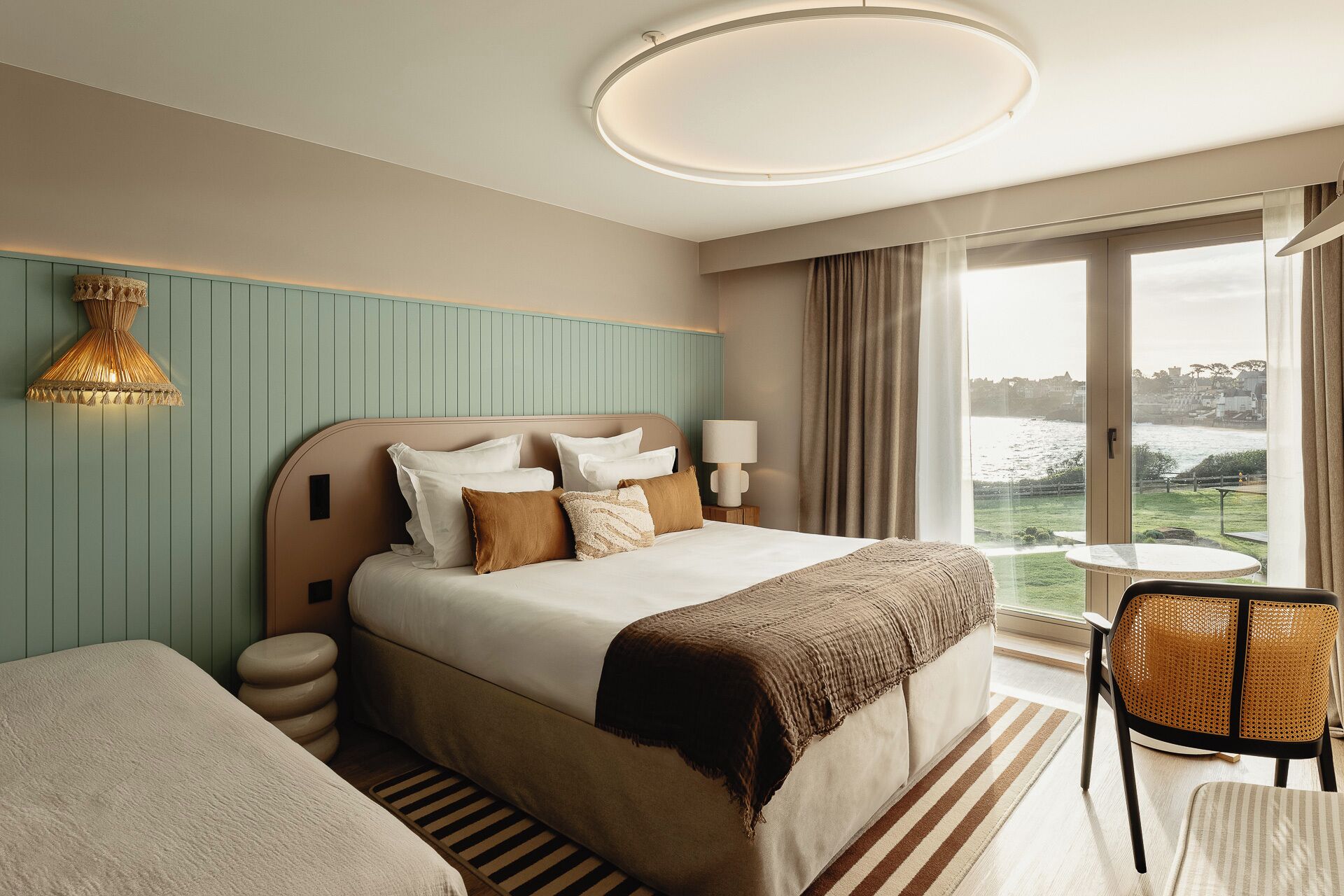 Habitación de hotel con cama, mesitas de noche, una silla, vistas al exterior y una lámpara de techo.