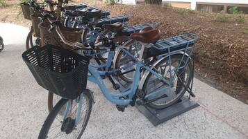 A blue bicycle with a basket and a kickstand, parked on a concrete surface.