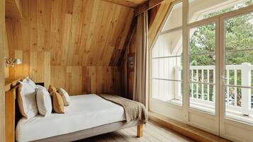 A bedroom with a wooden ceiling, a bed with pillows, a window with a view of trees, and a white fence outside.