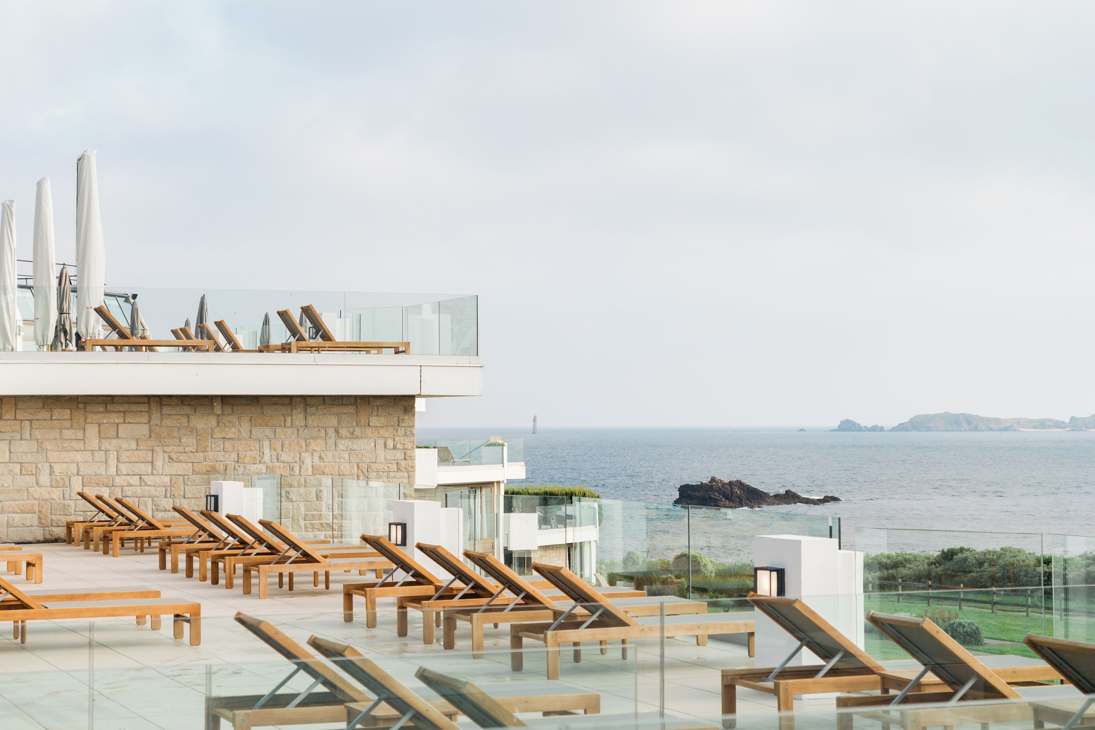 Un salon sur le toit, doté de chaises longues en bois et de parasols, offrant une vue sur la mer.