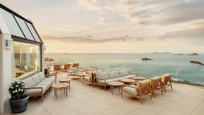 Une terrasse avec un canapé, des chaises et des tables, donnant sur la mer.