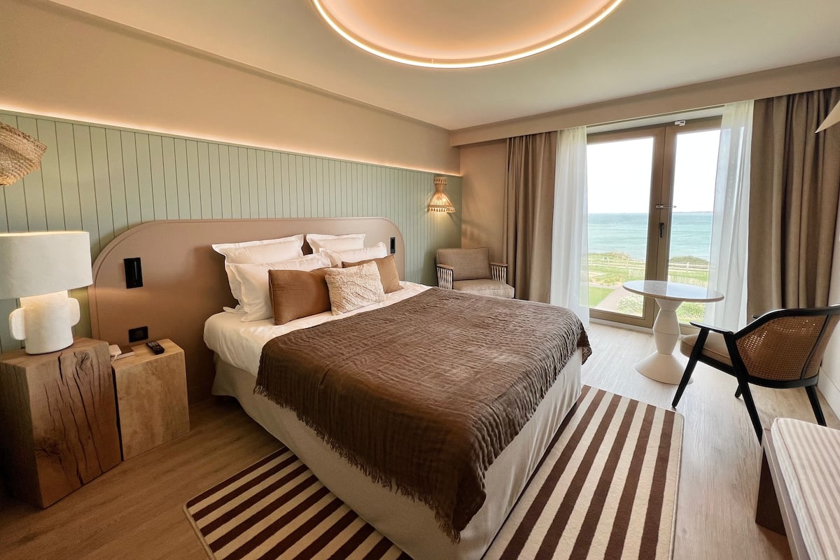 Une chambre d’hôtel moderne avec un grand lit, une table de chevet, une chaise et une vue sur la mer.