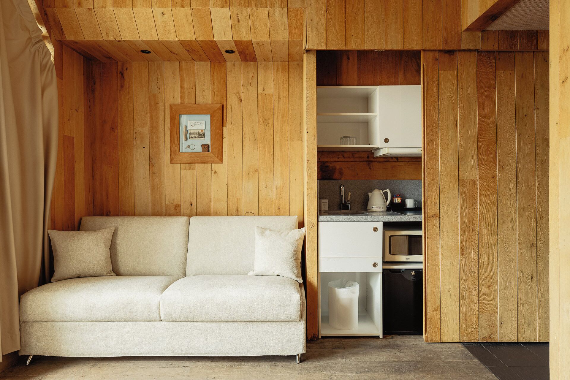 Una habitación acogedora con sofá, paredes de madera, un cuadro enmarcado y una kitchenette con cafetera.