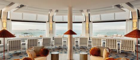 A spacious indoor area with multiple seating arrangements, large windows offering ocean views, and a central column.