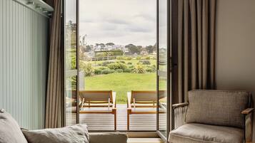 A room with a view of a garden, two wooden chairs, and a sofa.