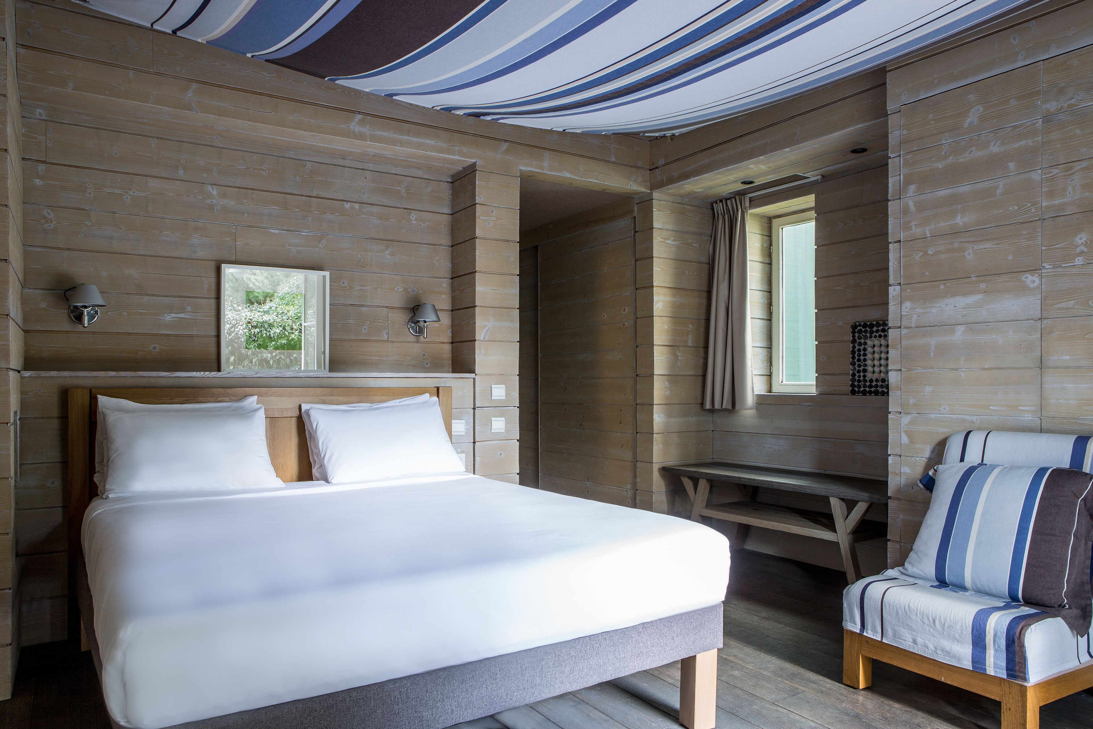 Un dormitorio con una cama grande, un banco de madera y un sillón a rayas.