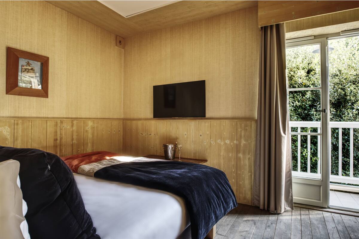 Une pièce avec un lit, une télévision, une fenêtre avec des rideaux et un mur en bois.