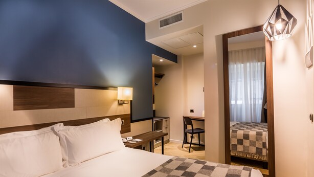 A hotel room with a large bed, a desk, and a chair. There is a mirror on the wall and a window with curtains. - Best Western Hotel Metropoli (Genoa)