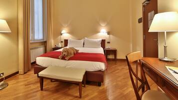 Een hotelkamer met een bed, nachtlampjes, een bureau, een stoel en een raam met gordijnen.