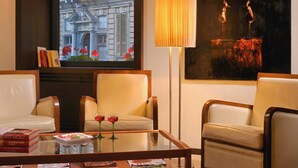 A hotel room with two leather armchairs, a glass coffee table with magazines, a large window with a view of a building, a tall floor lamp, and a painting on the wall. - Best Western Hotel Metropoli (Genoa)