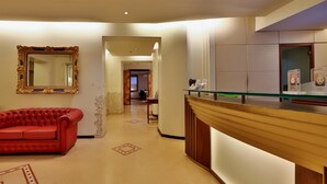 A hotel lobby with a red sofa, a reception desk, a large mirror, and a tiled floor. - Best Western Hotel Metropoli (Genoa)