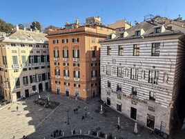 Un cortile con edifici storici, tra cui una banca e un palazzo con statue.