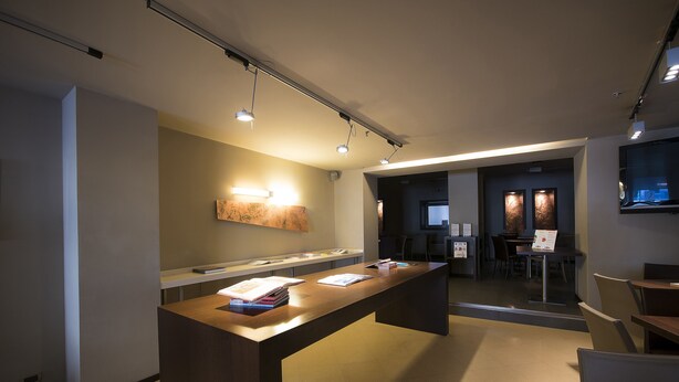 A modern reception area with a long reception desk, a wall-mounted light, and a seating area with tables and chairs. - Best Western Hotel Metropoli (Genoa)