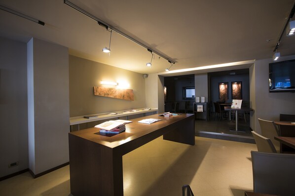 A modern reception area with a long reception desk, a wall-mounted light, and a seating area with tables and chairs. - Best Western Hotel Metropoli (Genoa)