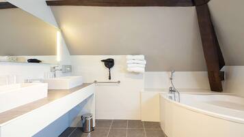A modern bathroom with a large bathtub, two sinks, a mirror, and a towel rack.
