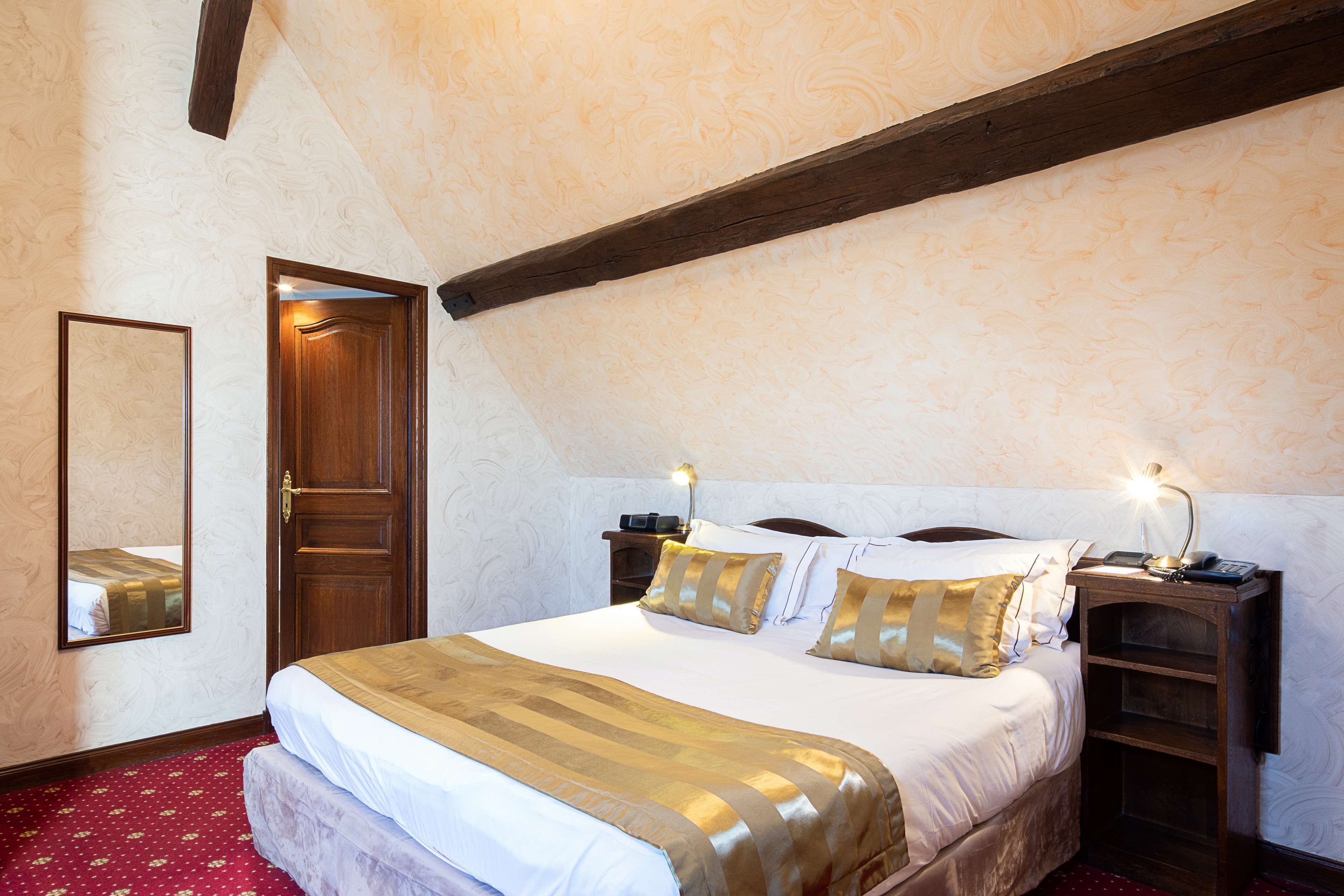 Ein ordentlich bezogenes Bett mit einer gestreiften Decke, ein Nachttisch aus Holz mit einer Lampe und ein Spiegel an der Wand.