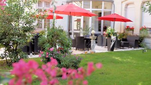An outdoor patio area with red umbrellas, wicker furniture, and a well-maintained lawn. - Best Western Central Hotel (Tours)