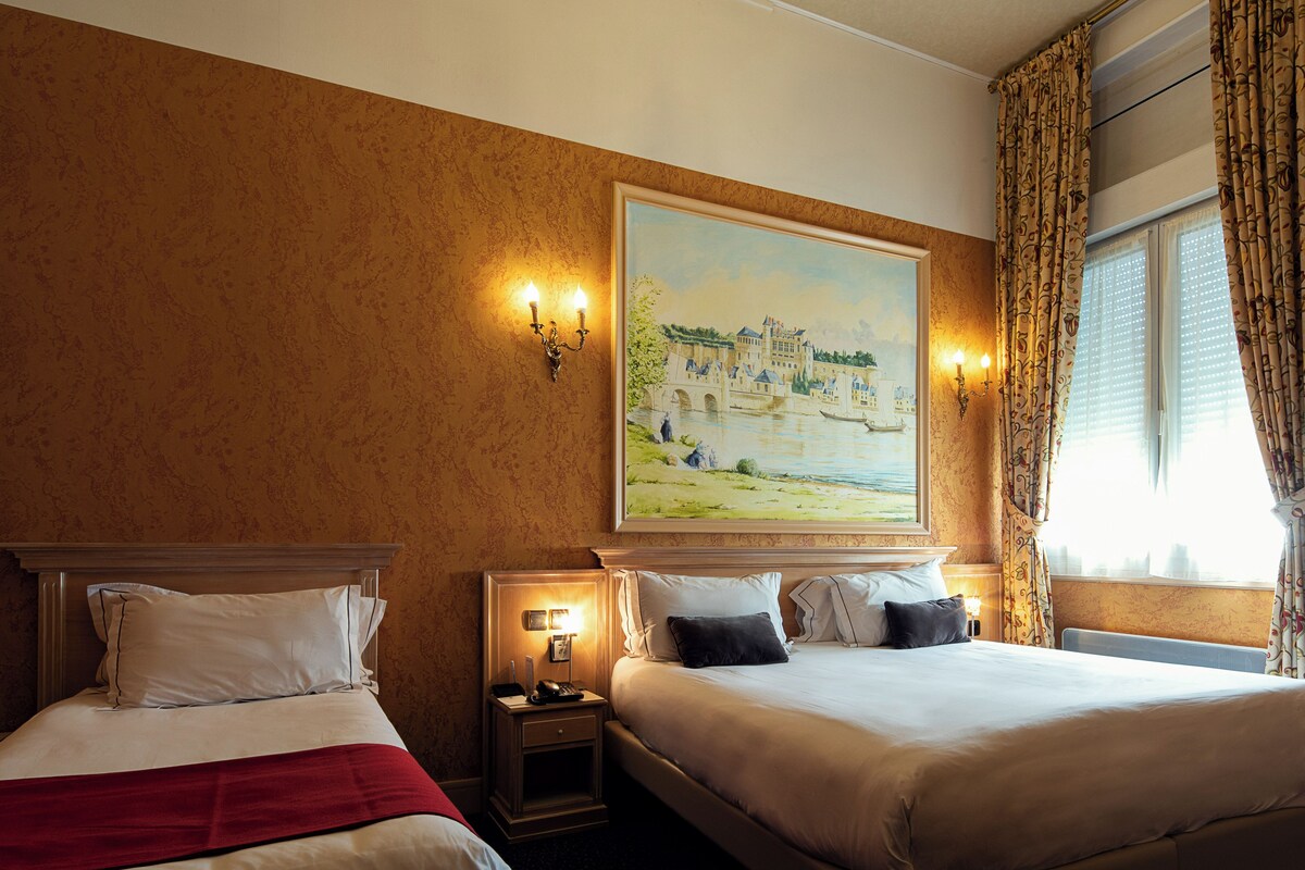 A hotel room with two beds, a painting of a castle, and a window with curtains.
