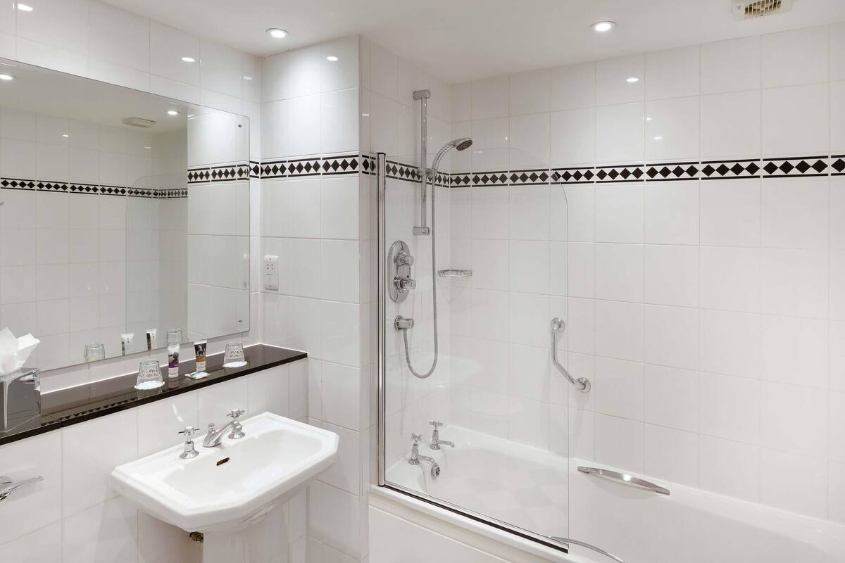 Un baño moderno con un lavabo blanco, ducha con mampara de cristal y un espejo grande sobre el lavabo.