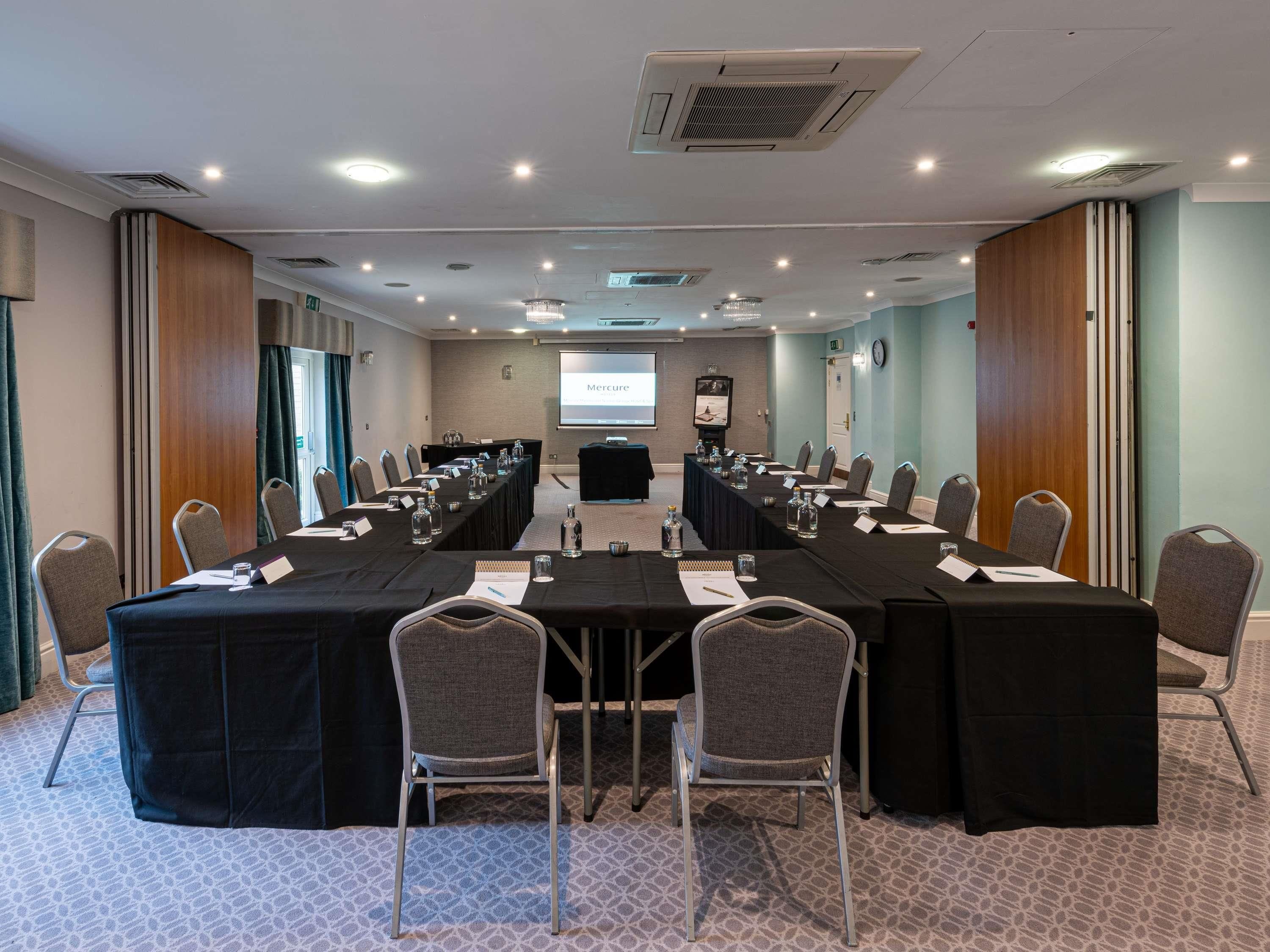 A conference room with a long table, chairs, a projector screen, and a presentation screen.