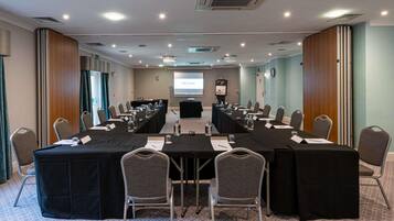 A conference room with a long table, chairs, a projector screen, and a presentation screen.