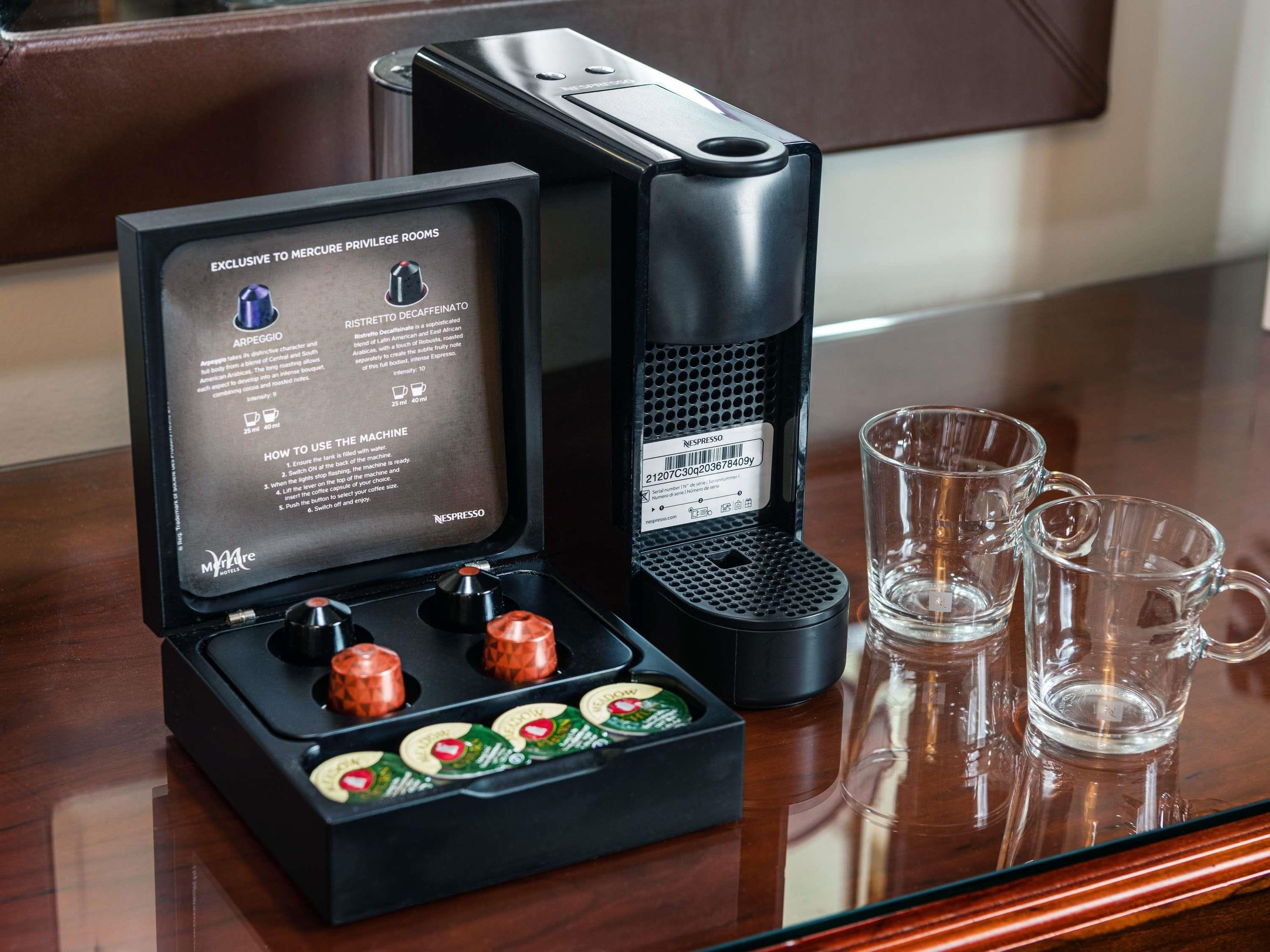 A Nespresso coffee machine with a coffee pod holder and three empty coffee cups on a wooden table.