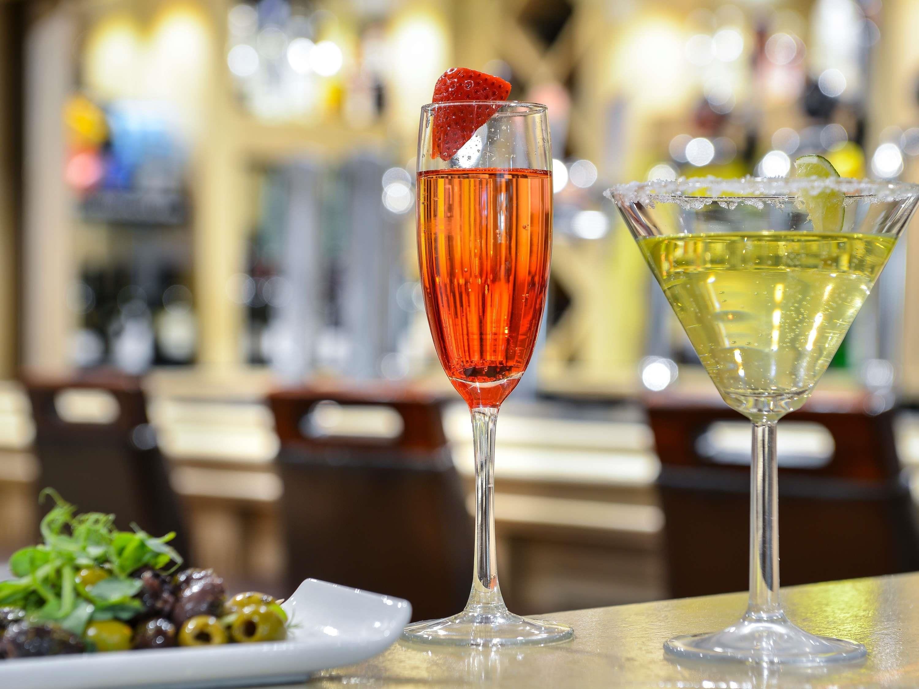 Two cocktails on a bar counter with a blurred background.