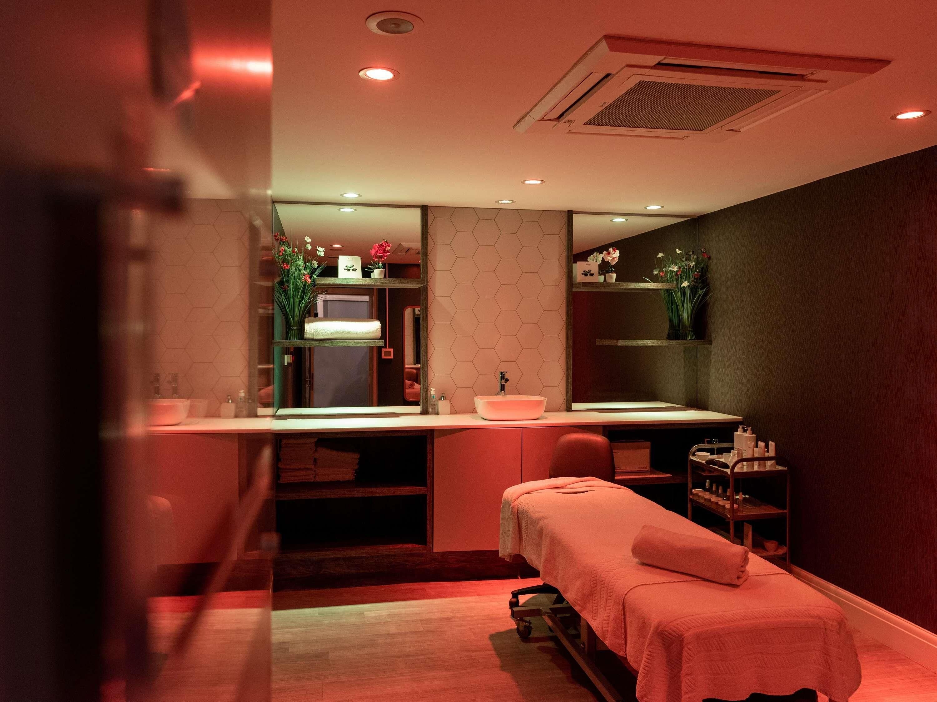 A modern bathroom with two sinks, a large mirror, and a massage table.