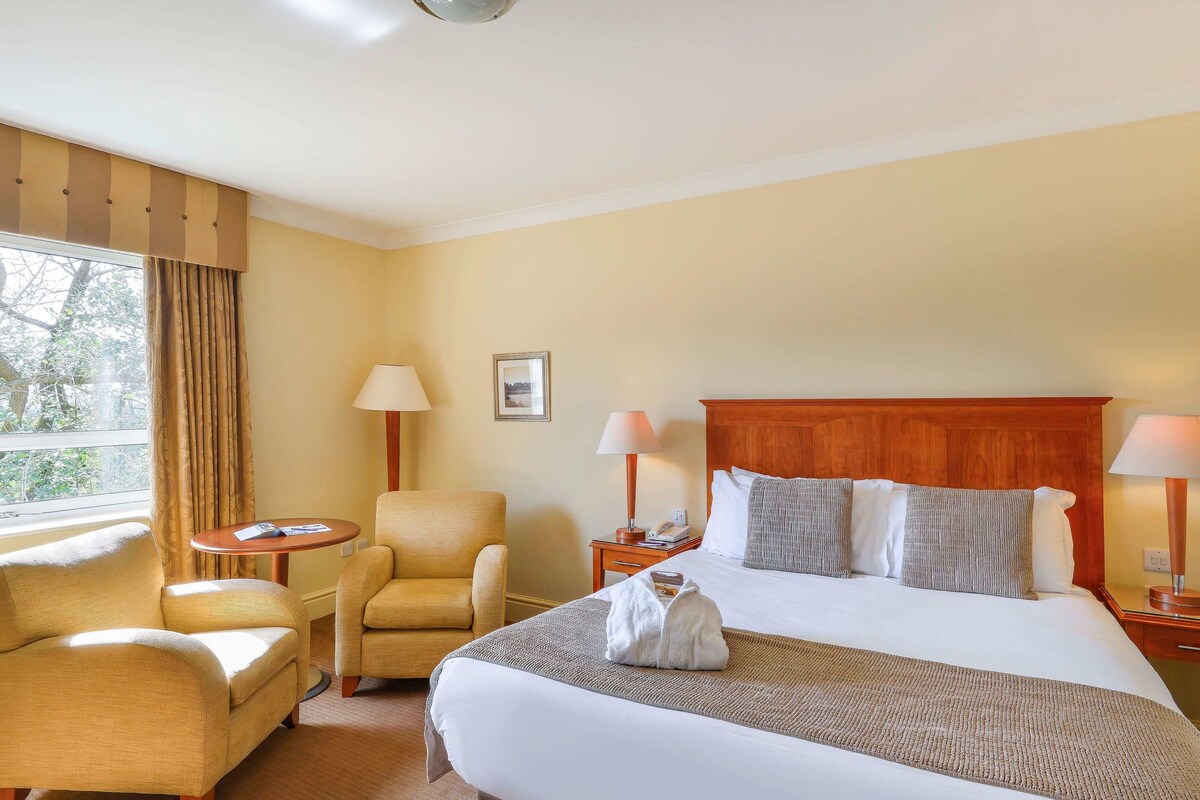 Una habitación de hotel con una cama grande, una silla, una mesita y una lámpara.