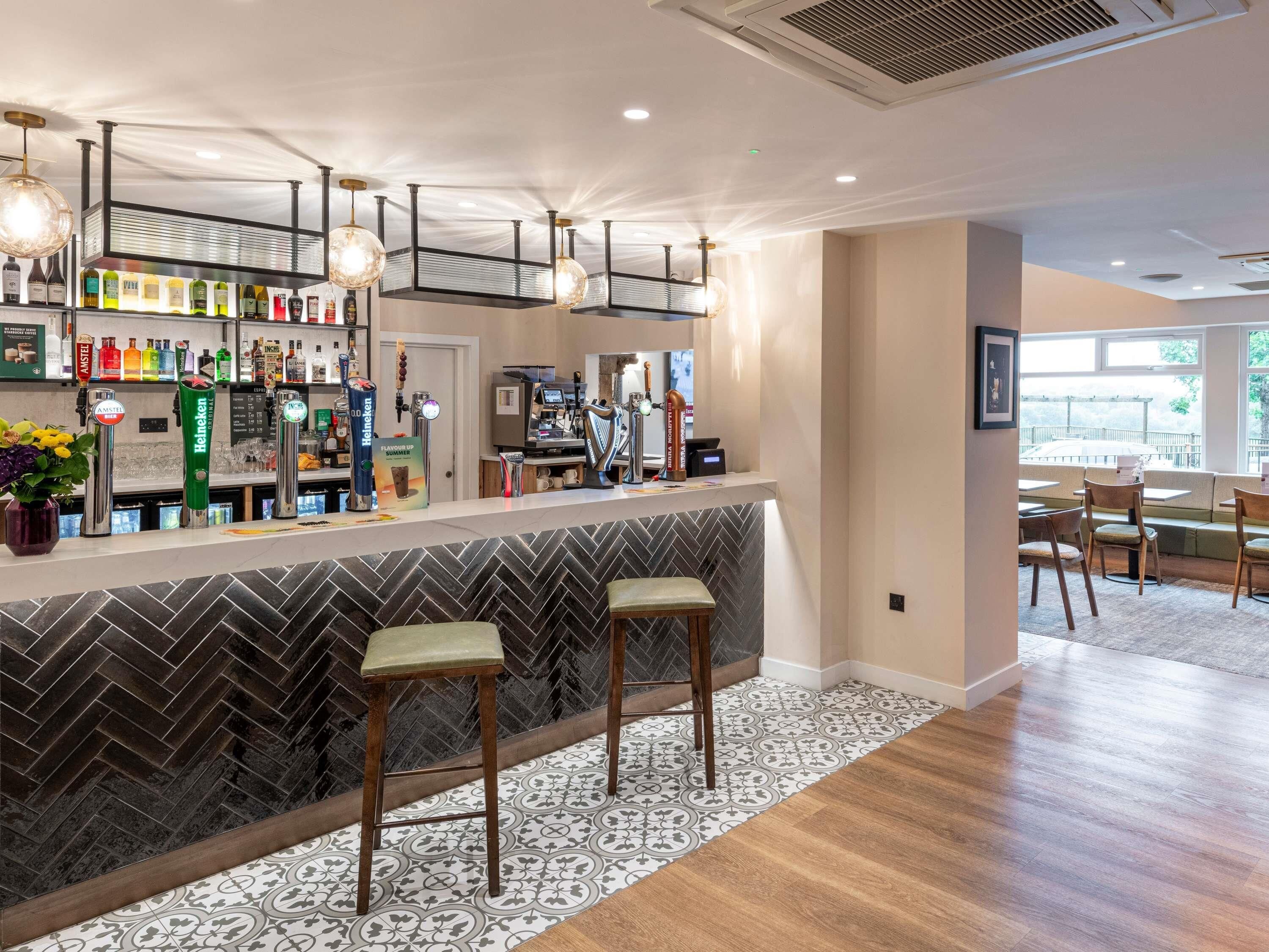 Zona de bar con taburetes, una barra y una variedad de botellas.