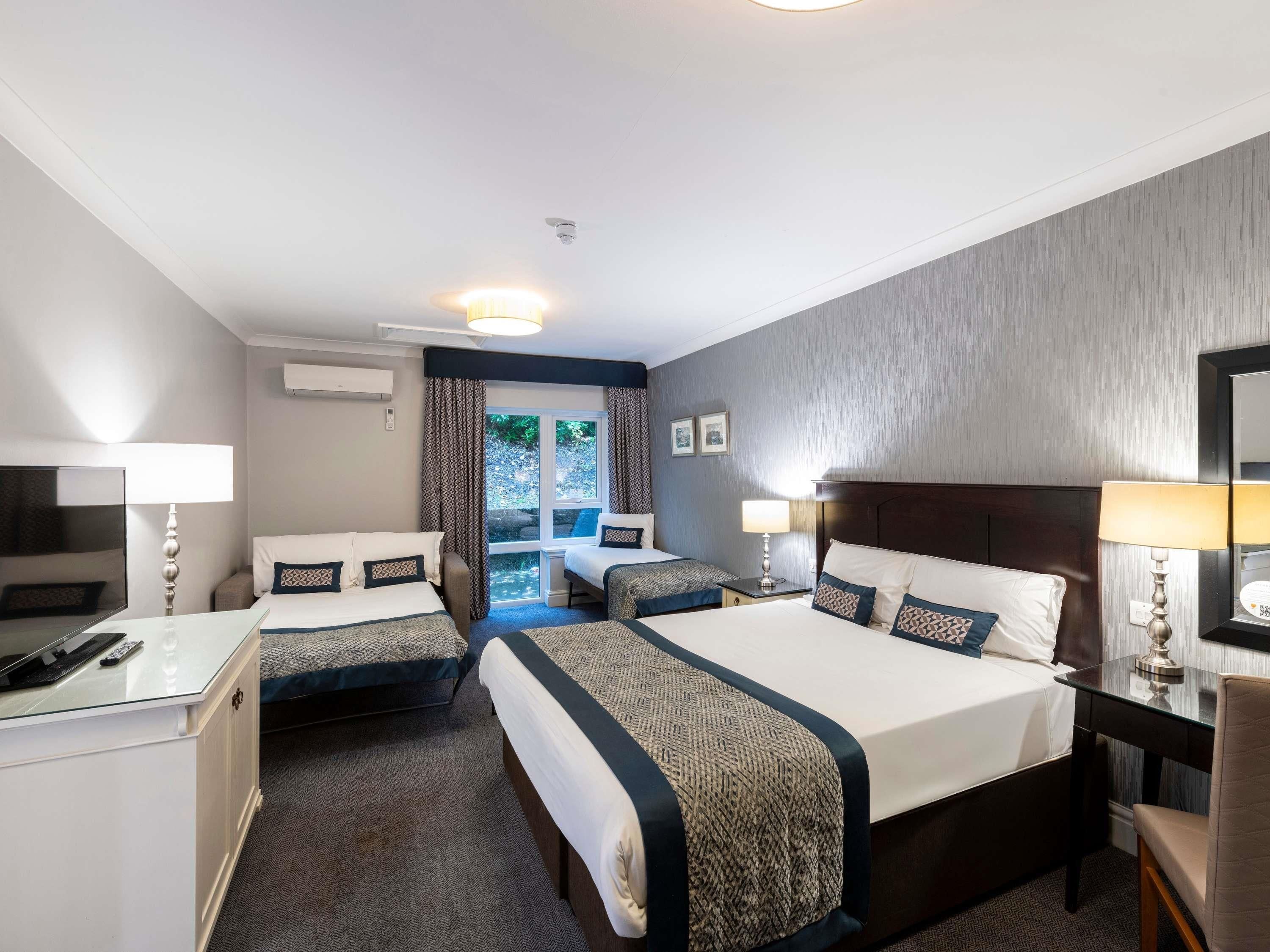 Habitación de hotel con dos camas, un escritorio, una silla y una ventana con cortinas.