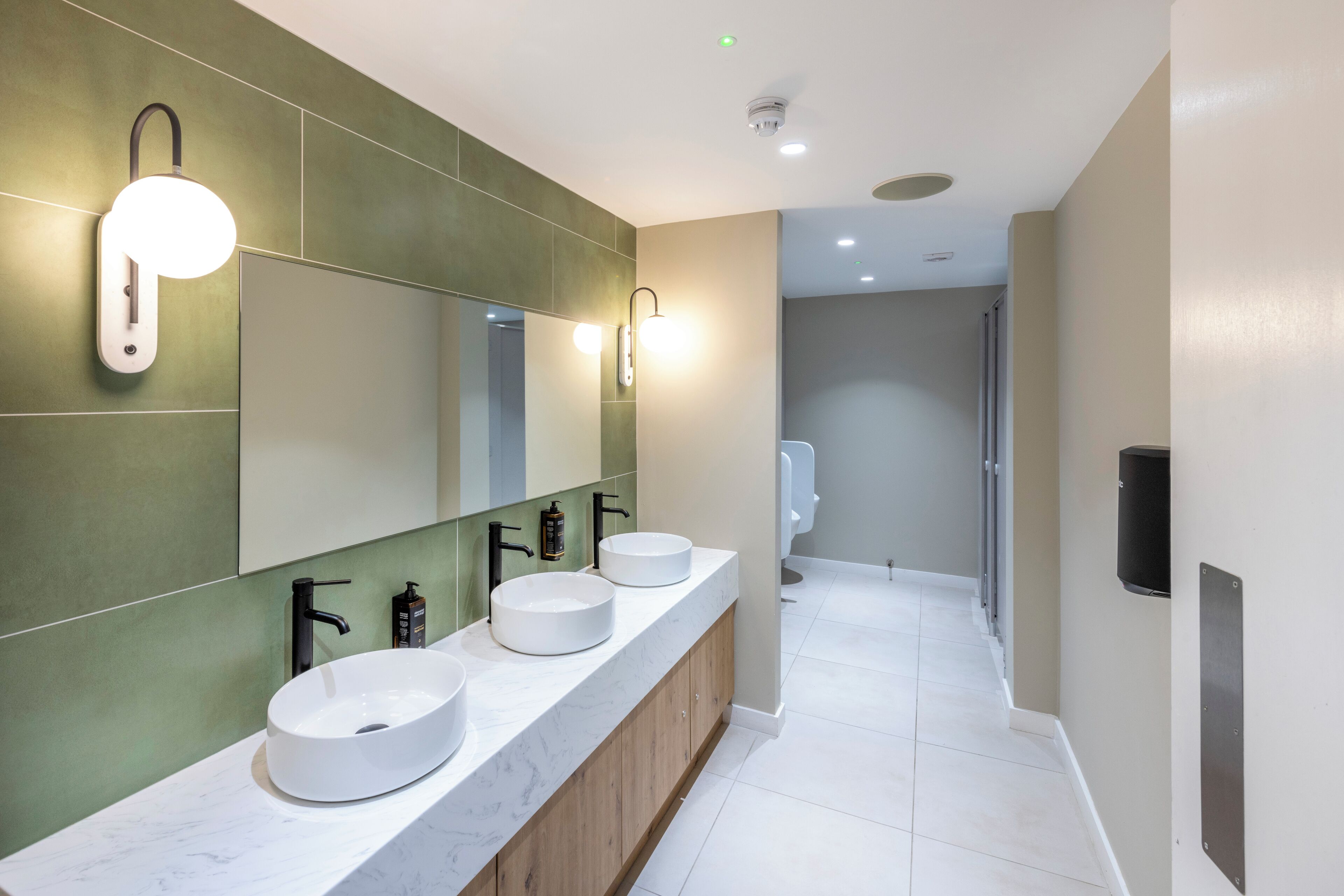 Un baño moderno con un tocador amplio, tres lavabos redondos y un espejo grande.
