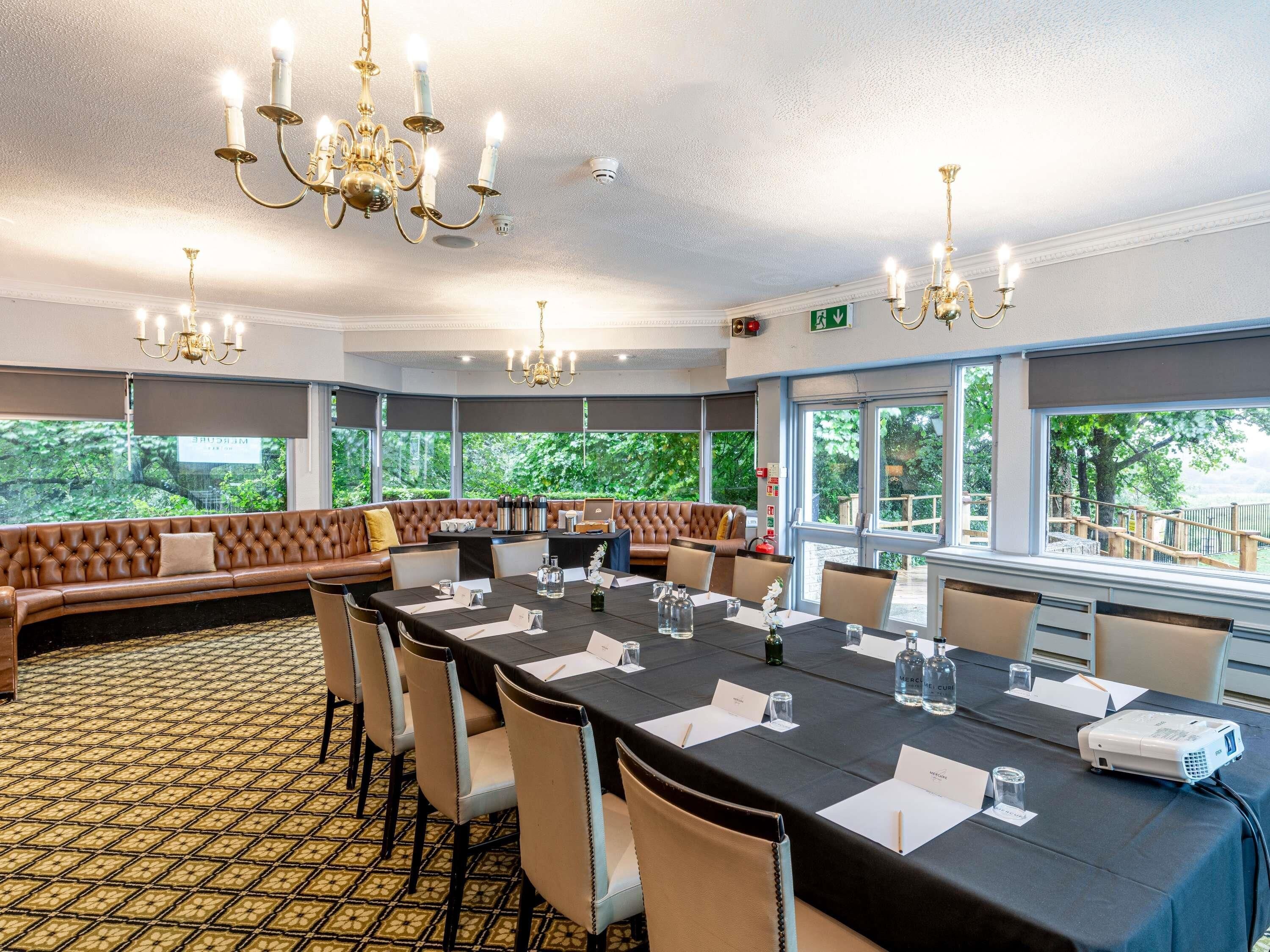 A conference room with a long table, chairs, a projector, and a large window with a view of greenery.