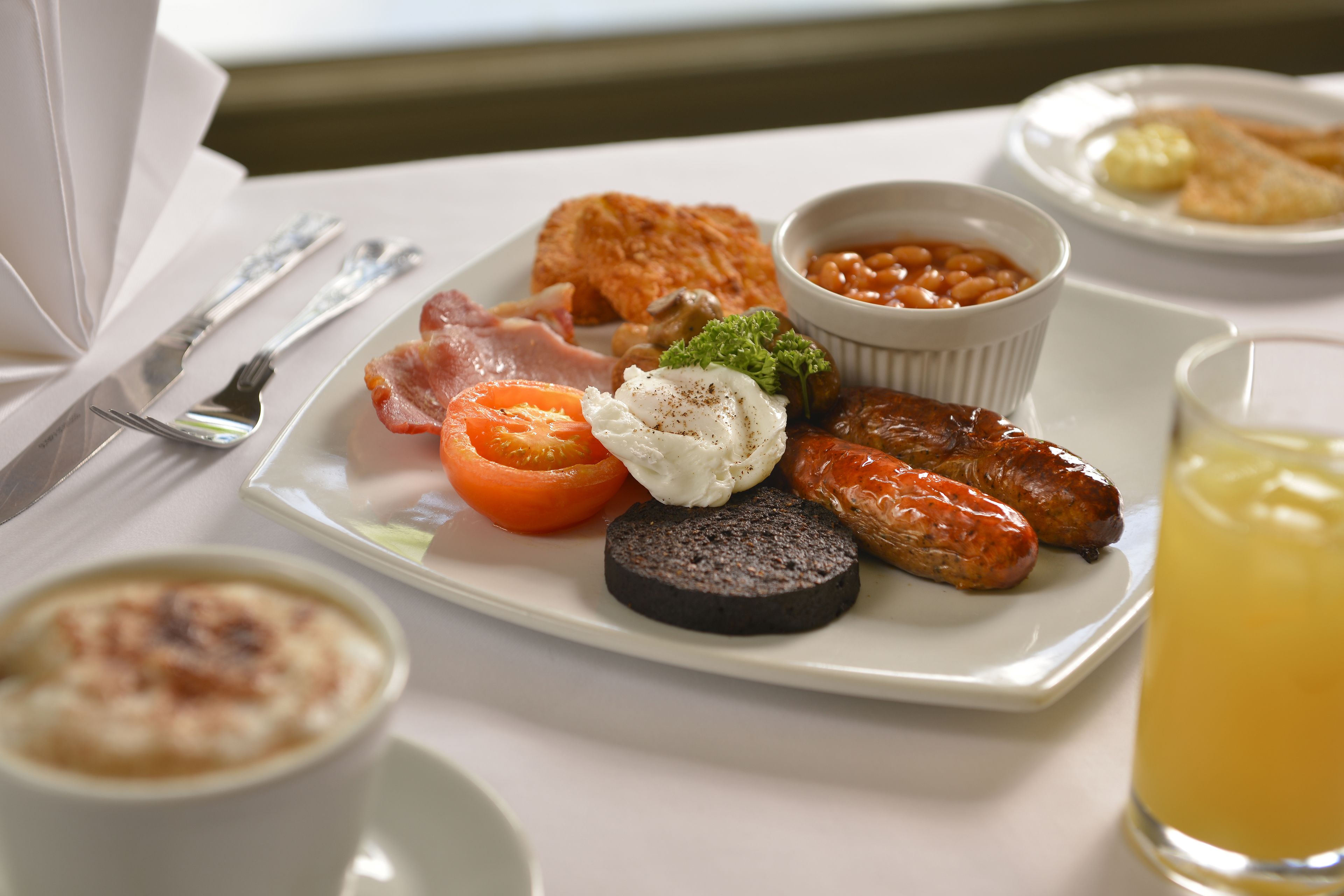 Un plato de desayuno con huevos, tocino, salchichas, tomates y frijoles.