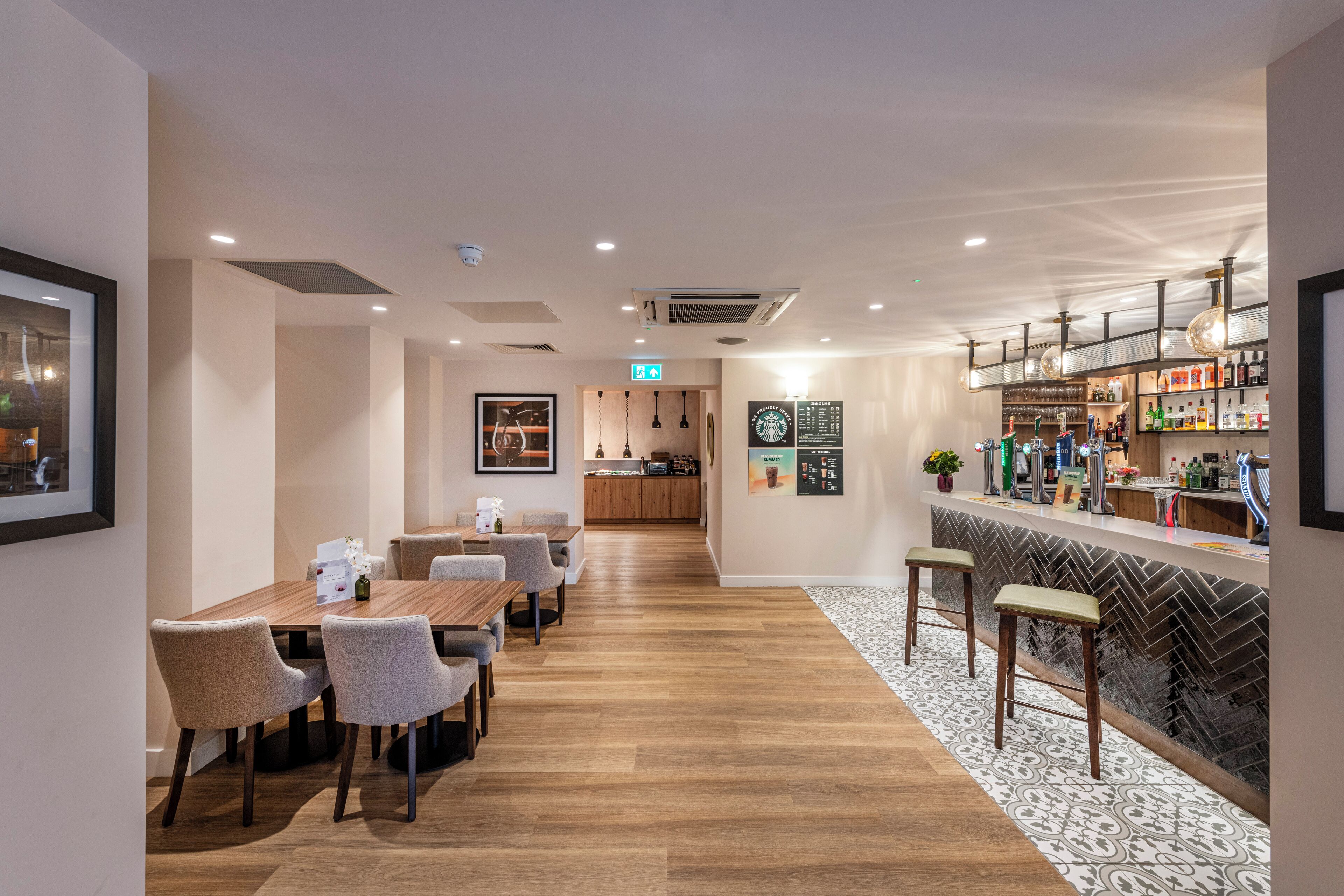 A modern hotel lobby with a wooden reception desk, seating area, and a bar.