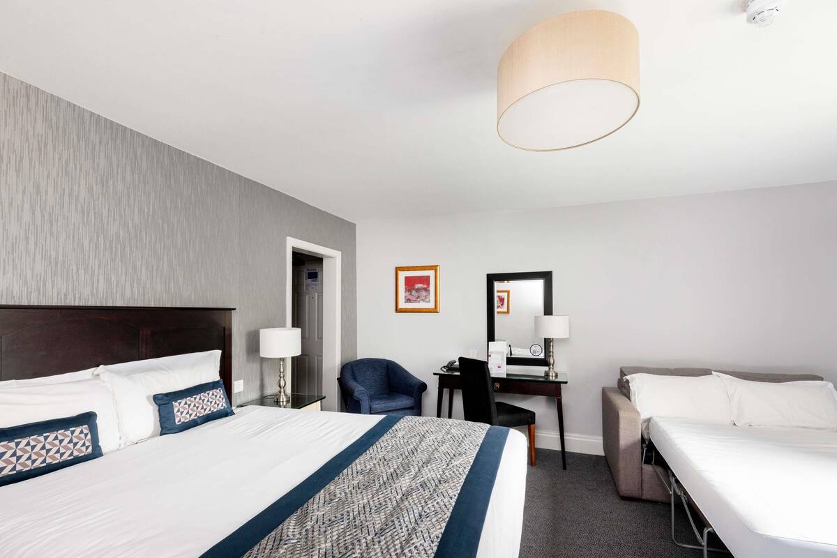 Habitación de hotel con una cama grande, un escritorio con silla, una lámpara de escritorio, una mesa de noche.