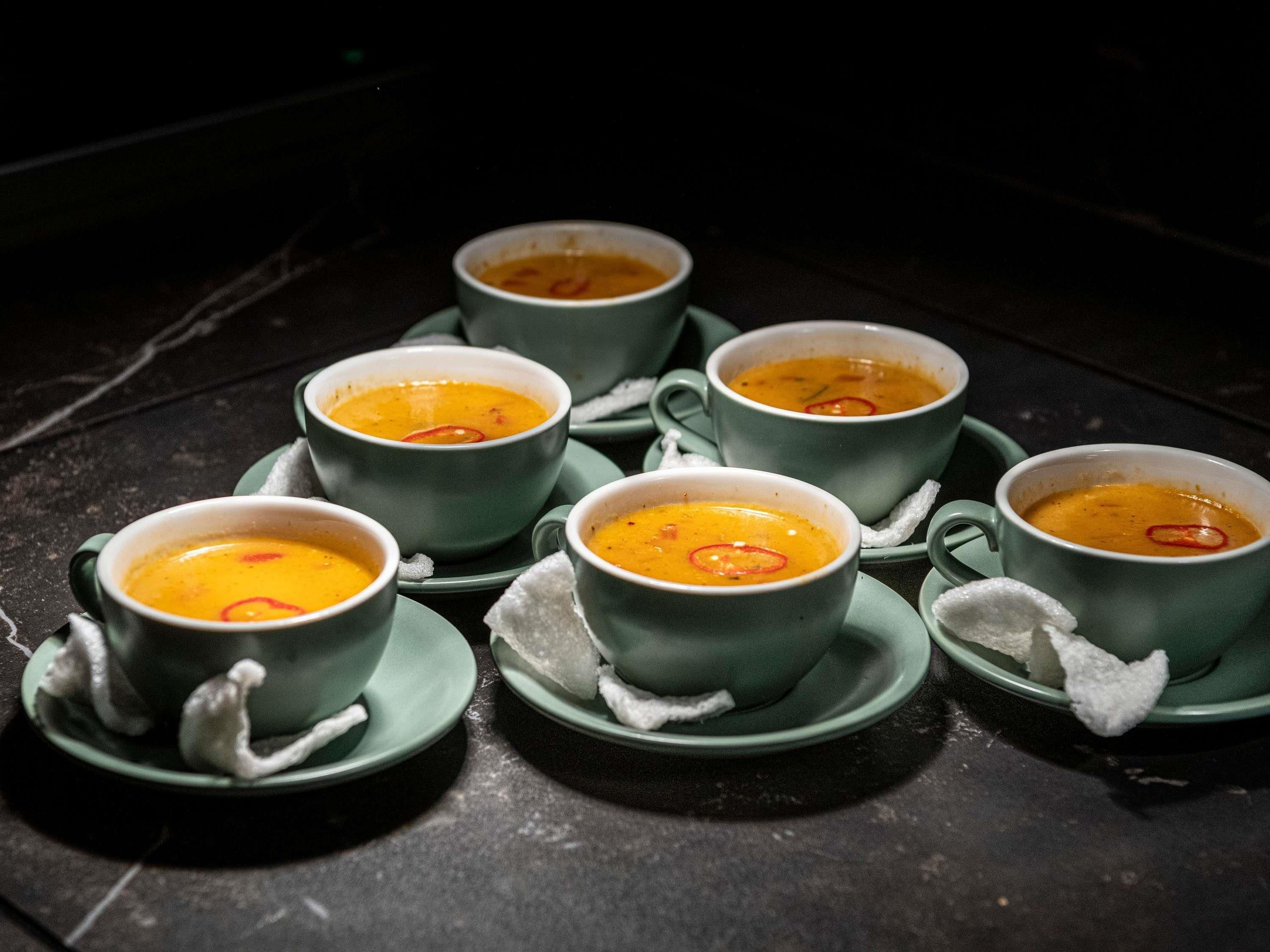 A table with six bowls of soup on matching green saucers.