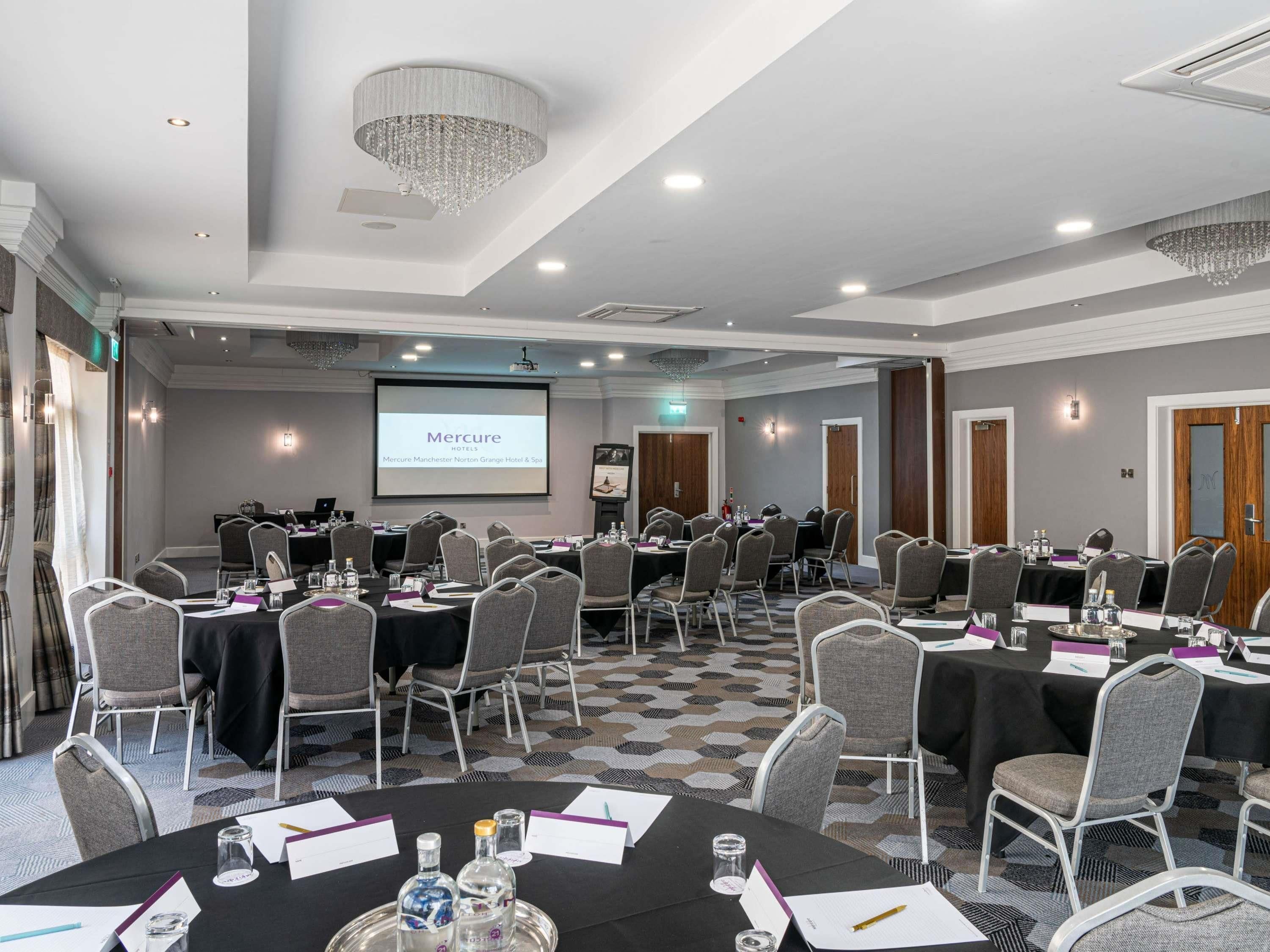 A conference room with round tables, chairs, a projector screen, and a chandelier.