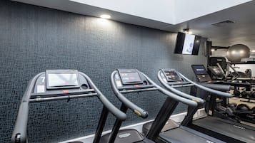 Tres cintas de correr en un gimnasio con una pared texturizada y un televisor montado.