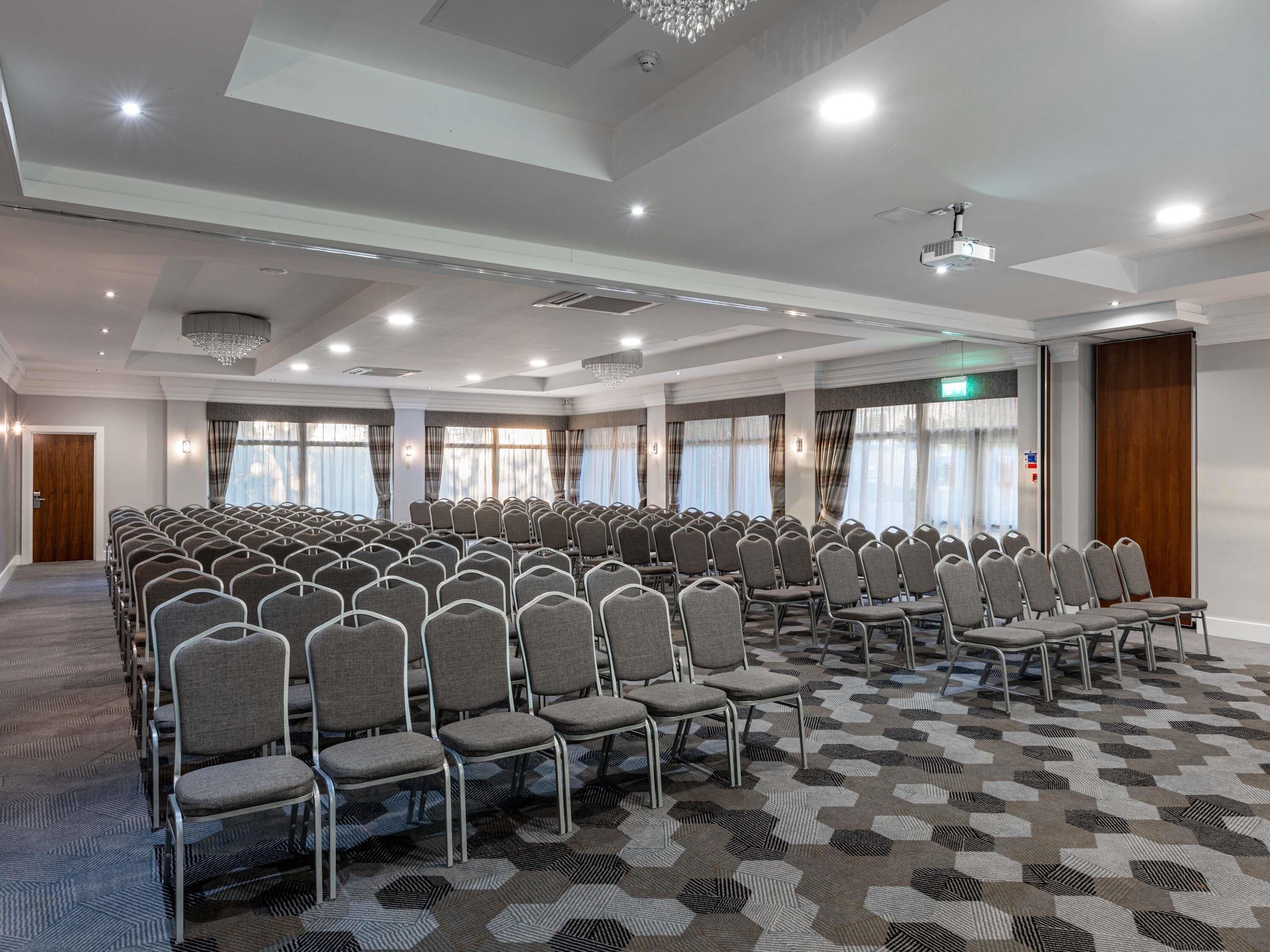 A conference room with rows of chairs, a patterned carpet, and a chandelier.