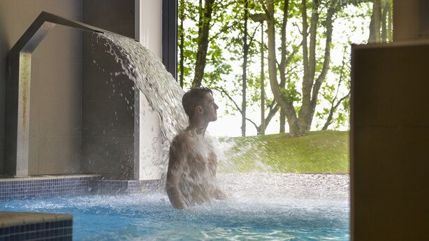 Eine Person in einem Schwimmbecken, Wasser fließt von einer Struktur herab.