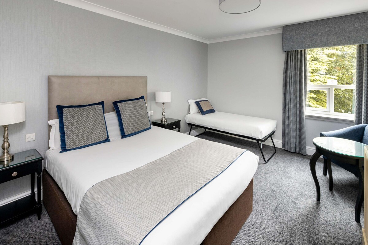 Une chambre d’hôtel avec un grand lit, un lit plus petit, un bureau et une chaise.