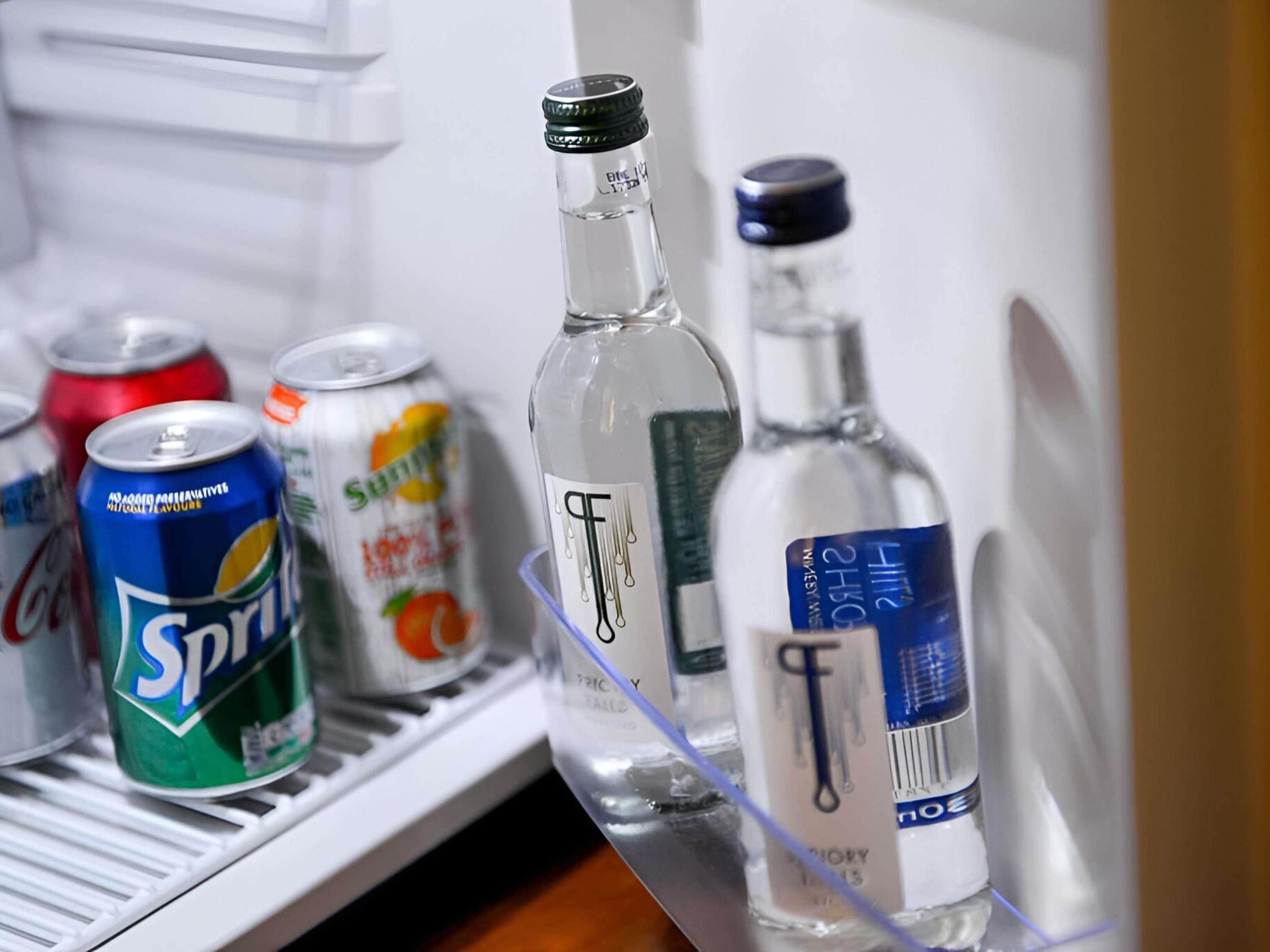 A refrigerator with beverages including a Sprite can, a bottle of water, and a bottle of alcohol.